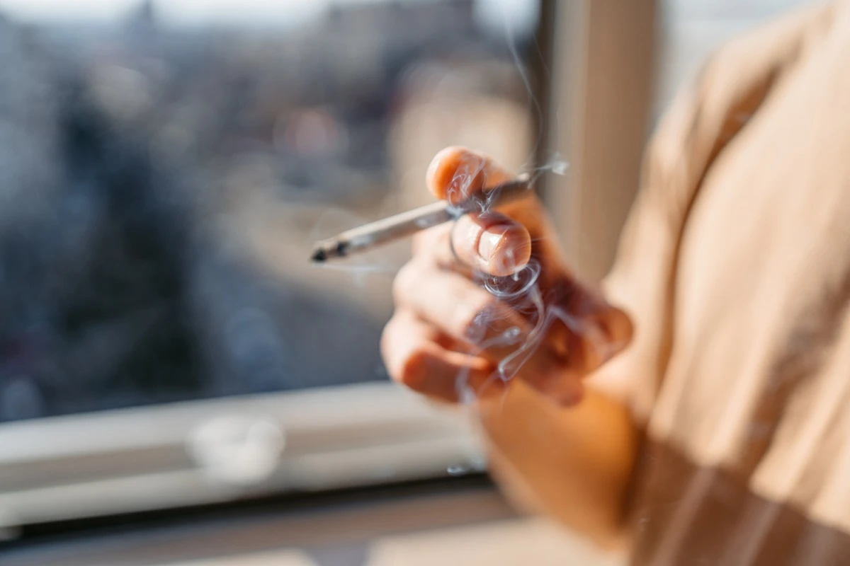 1 de 1 Close de um jovem/adolescente em pé perto da janela fumando um cigarro em casa. Metrópol...