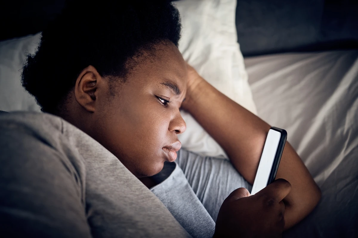 Imagem mostra mulher negra olhando o celular na cama - Entenda por que assistir vídeos acelerado...