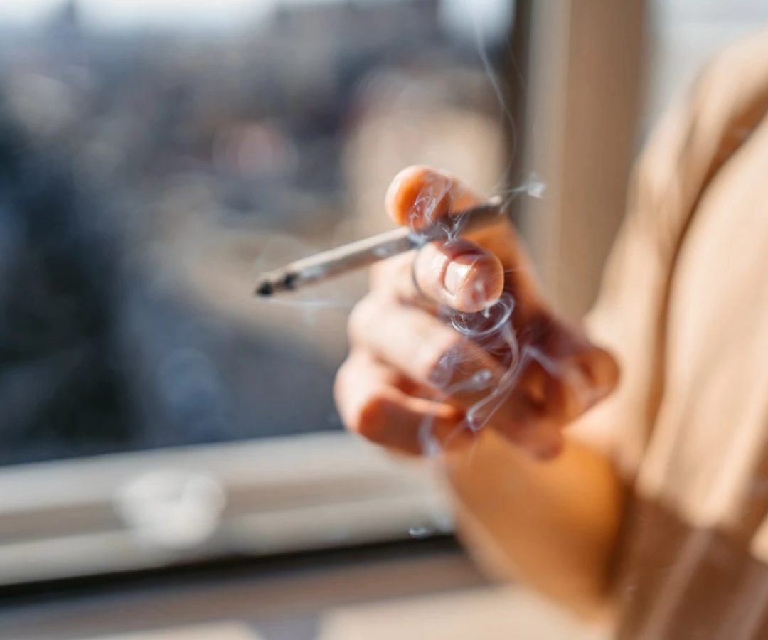 1 de 1 Close de um jovem/adolescente em pé perto da janela fumando um cigarro em casa. Metrópol...