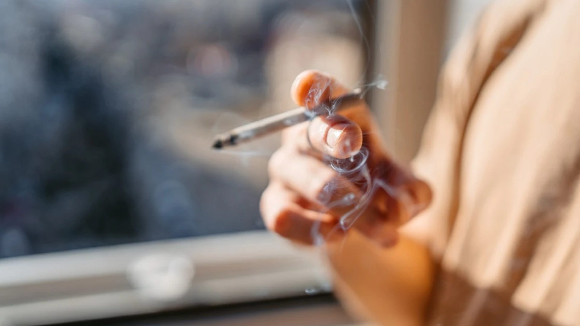 1 de 1 Close de um jovem/adolescente em pé perto da janela fumando um cigarro em casa. Metrópol...