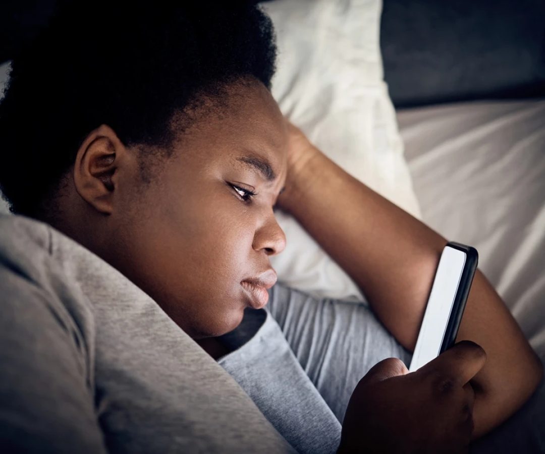 Imagem mostra mulher negra olhando o celular na cama - Entenda por que assistir vídeos acelerado...