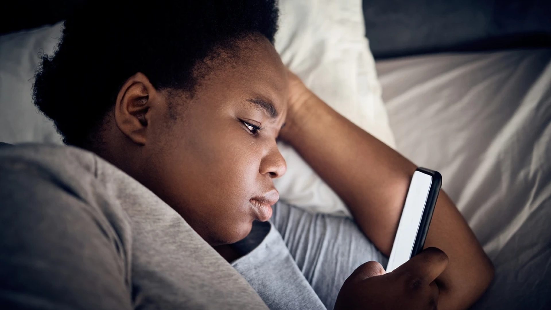 Imagem mostra mulher negra olhando o celular na cama - Entenda por que assistir vídeos acelerado...